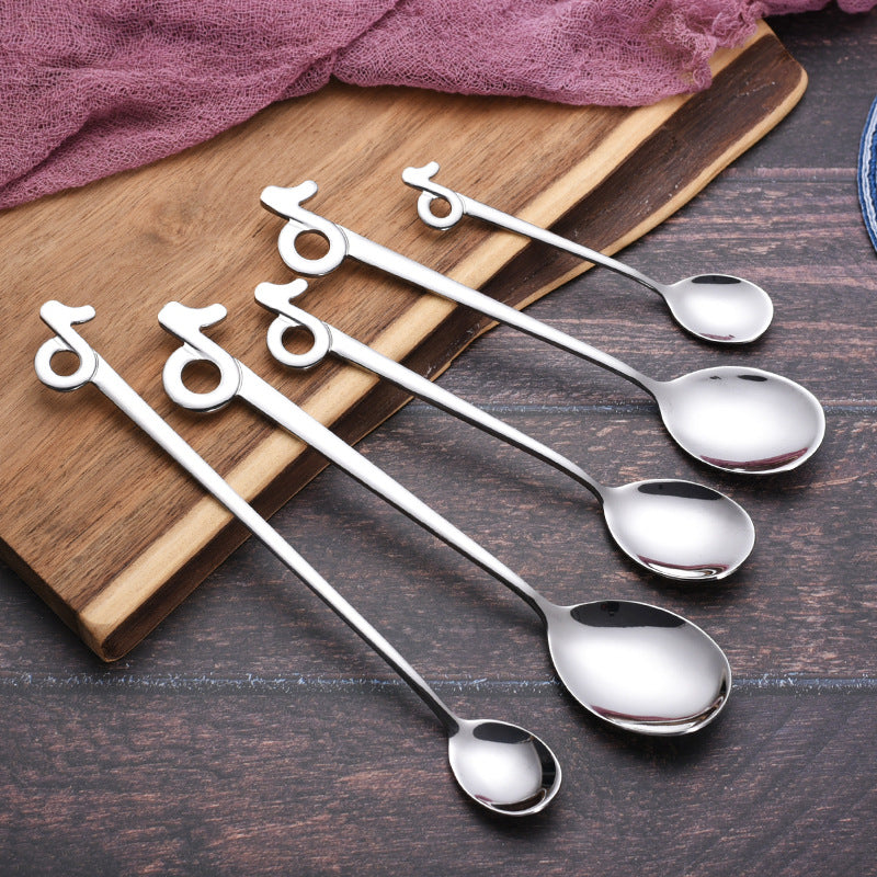 Five silver musical-note spoon styles displayed diagonally across a wooden board and dark table