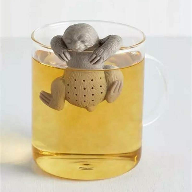 Sloth-shaped tea infuser suspended inside a tall clear glass mug of golden tea on a white background