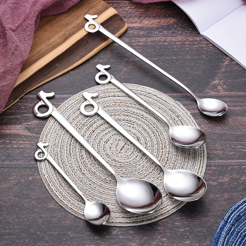 Five musical-note stainless steel spoon styles arranged on a round woven mat and dark wooden table